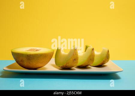Melone affettato su un piatto. Sfondo giallo e blu. Foto Stock