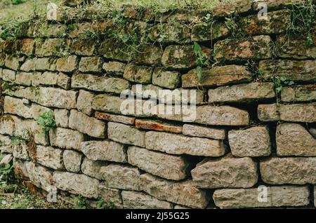 Parete lastricata con texture ruvida e chiara e linee profonde tra le grandi pietre. Posa vecchia recinzione. Distrutto recinto di pietra. Foto Stock