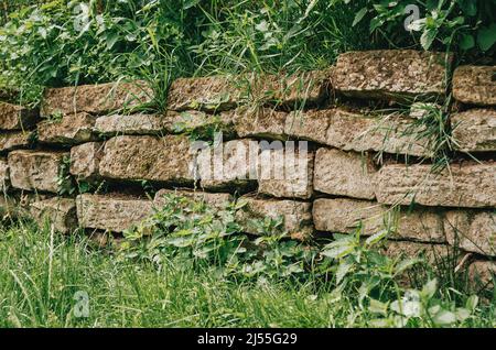 Recinzione di pietra, coltivata con muschio e erba. Tessitura di pietra. Architettura obsoletata. Vista laterale Foto Stock