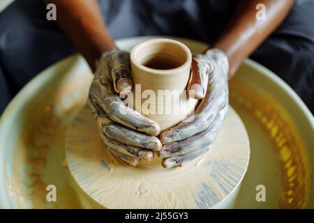 misto di razza afro maschio vasaio con grembiule nero seduto al vasaio da tavolo da officina Foto Stock