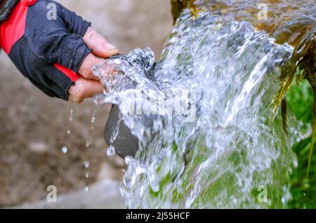 Il flusso di acqua di sorgente pura. La mano dell'uomo raccoglie l'acqua in una tazza in una sorgente di cristallo fresco. Foto Stock