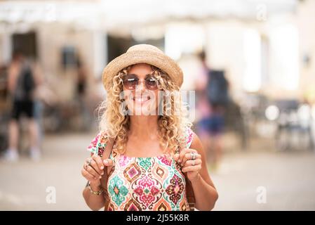 Ritratto di allegro bella giovane donna adulta sorridente e guardando la macchina fotografica. Buon turista con zaino. Donne alla moda con occhiali da sole e def Foto Stock