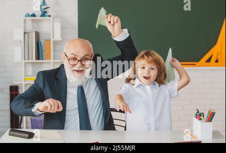 Insegnante senior o nonno e allievo del ragazzo della scuola tengono l'aeroplano di carta in aula alla scuola. Lezione privata divertente. Foto Stock