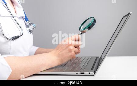 Lente di ingrandimento da medico sullo schermo del computer portatile. Consulenza medica online e concetto di controllo. Analisi approfondita dei reclami dei pazienti a distanza. Foto di alta qualità Foto Stock