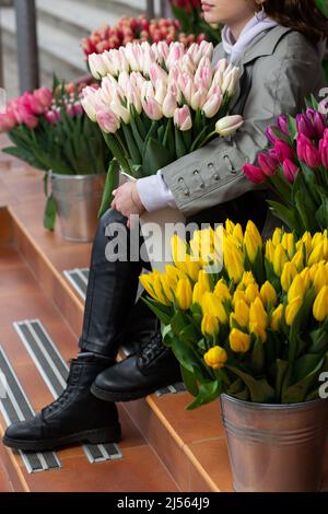 Tulipani rosa in mano donna. Giovane bella donna che tiene un bouquet di primavera su sfondo di fiori. Mazzo di fiori freschi di primavera in mano femmina Foto Stock