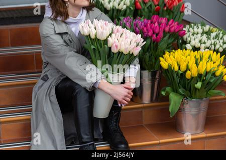 Tulipani rosa in mano donna. Giovane bella donna che tiene un bouquet di primavera su sfondo di fiori. Mazzo di fiori freschi di primavera in mano femmina Foto Stock