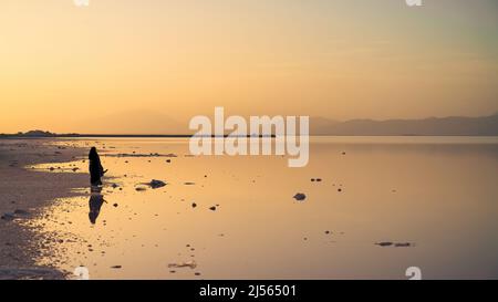 Shiraz, Iran - Maggio 2019: Donna iraniana velata in abito nero hijab seduto su una roccia vicino al lago rosa Maharloo Foto Stock