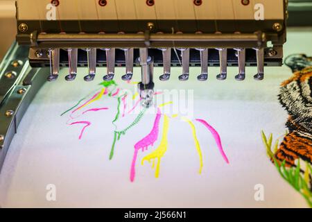 Aghi di una macchina da ricamo industriale e tessuto con punti di filo multicolore in primo piano Foto Stock