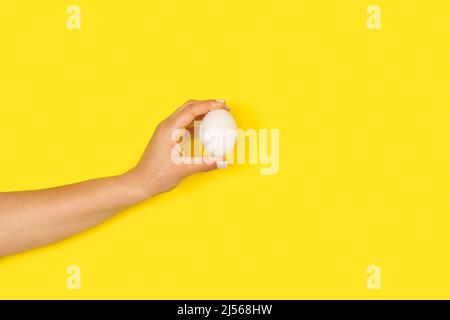 Mano donna che tiene un uovo di pollo su uno sfondo giallo con spazio copia Foto Stock