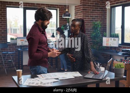 Donna d'affari in attesa che usa il computer moderno per rivedere la politica di lavoro della startup società. Diversi uffici multiculturali che parlano di strategie redditizie e di portfolio di partner. Foto Stock