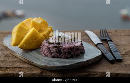 Frutta fresca di mango gialla matura (Barracuda mango) e foglia di panda con aggiunta di frutti di bosco riceberry su piastra di ceramica servita con coltello e forchetta. Messa a fuoco selettiva. Foto Stock