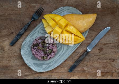 Frutta fresca di mango gialla matura (Barracuda mango) e foglia di panda con aggiunta di frutti di bosco riceberry su piastra di ceramica servita con coltello e forchetta. Messa a fuoco selettiva. Foto Stock