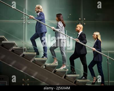 Multinazionale e multietnica corporate business persone maschio e femmina salendo le scale in una linea in un ufficio moderno edificio. Foto Stock