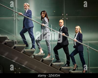 multinazionale e multietnico business persone maschio e femmina che saliscono le scale in una fila guardando la macchina fotografica in un moderno edificio d'ufficio. Foto Stock