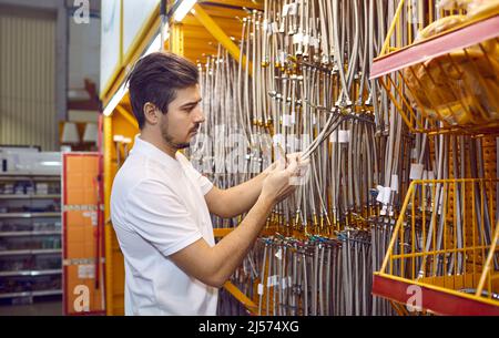 L'uomo in negozio sceglie tubi flessibili per l'acqua con beccuccio in metallo per il collegamento di attrezzature idrauliche. Foto Stock