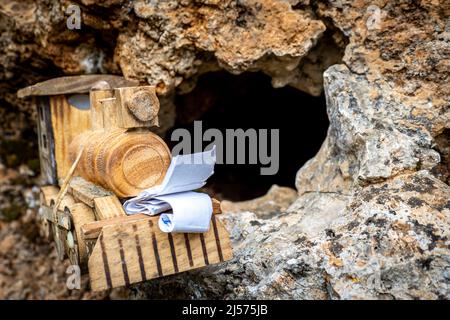 Disposizione di una scoperta di geocaching riuscita. Un piccolo contenitore di geocaching di locomotiva giocattolo con un giornale di bordo nascosto in un buco di roccia Foto Stock