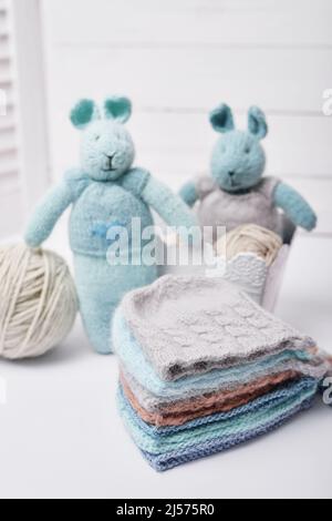 Lavoro a maglia e a maglia. Hobby e creatività. Maglia per bambini. Giocattoli a maglia coniglio e cappello. Lepre giocattolo fatto a mano. Berretto bambino. Filati, fili e palle. Foto Stock