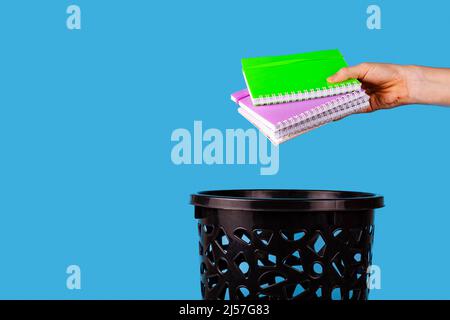 I notebook vengono gettati nel cestino. Per spazio di copia per i designer su sfondo blu. Foto Stock