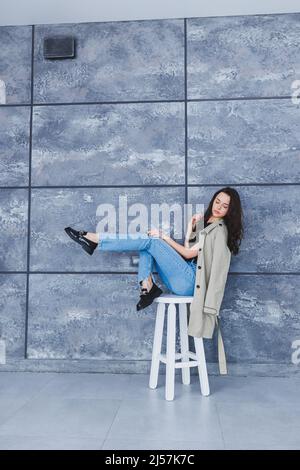 Bella donna con gambe sottili in jeans e outerwear alla moda con un impermeabile, scarpe eleganti in pelle. Immagine femminile in stile primaverile Foto Stock