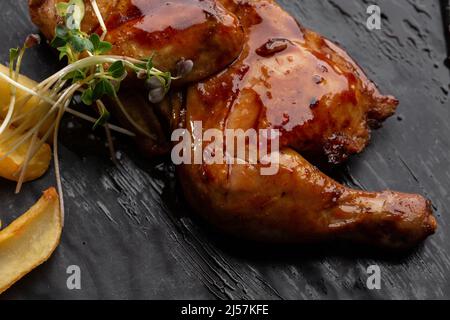 Carcassa di quaglia alla griglia con patatine fritte sul piatto su sfondo di pietra nera. Quaglie arrosto sul piatto. Vista dall'alto, piatto. Foto Stock