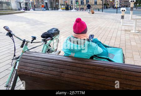 Black femmina addetto alla consegna della bicicletta che riposa e controlla le sue posizioni nel centro di Liverpool Foto Stock