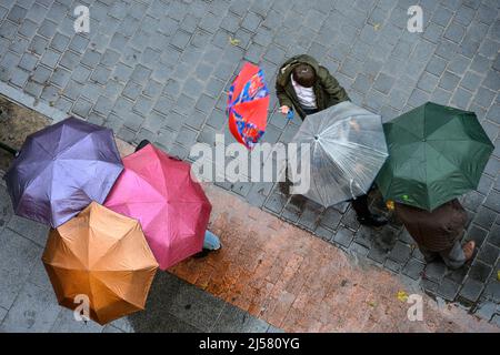 Gruppi di persone che parlano sotto gli ombrelloni in una giornata di pioggia a Madrid, Spagna. Foto Stock