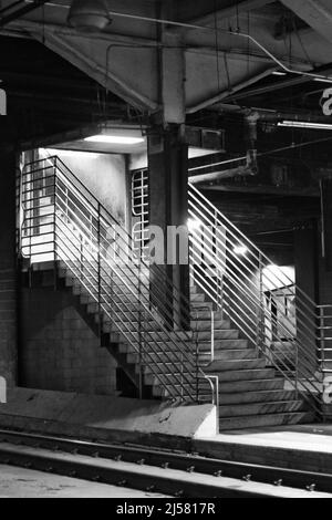 Scale pubbliche che saliscono al piano superiore dalla piattaforma della stazione in bianco e nero. Foto Stock