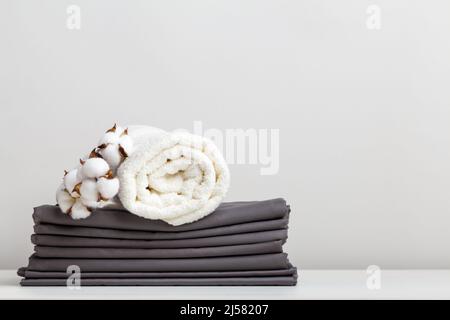 Una pila di lenzuola grigie, lenzuola e un asciugamano bianco spugna sul tavolo. Foto Stock