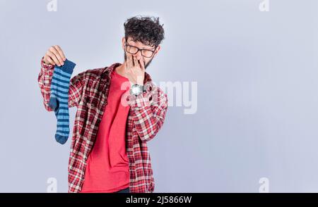 Un uomo con un calzino in mano che copre il naso, un ragazzo con un calzino stinky in mano, puzzolente calzini concetto Foto Stock