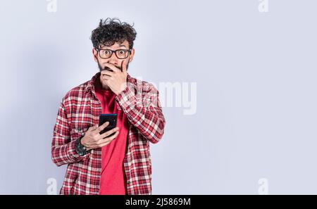 Giovane uomo con il suo cellulare che copre la bocca, concetto di un uomo stordito con il suo cellulare Foto Stock