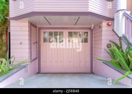 Esterno garage con porta doppia incernierata laterale e lap in legno rosa a San Francisco, California. Ci sono piante sul lato del vialetto headi Foto Stock