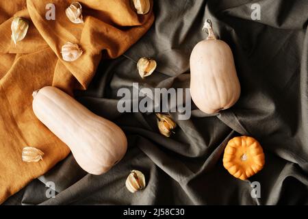 Vista ad alto angolo di phisalises con foglie secche chiuse e zucche allungate e rotonde su tessuti arancioni e grigi Foto Stock