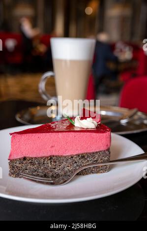 Pezzo di famosa torta di semi di papavero con mousse di lamponi di origine austriaca servito con panna montata e una tazza di caffè latte in vecchio classico caffè-ristorante Foto Stock