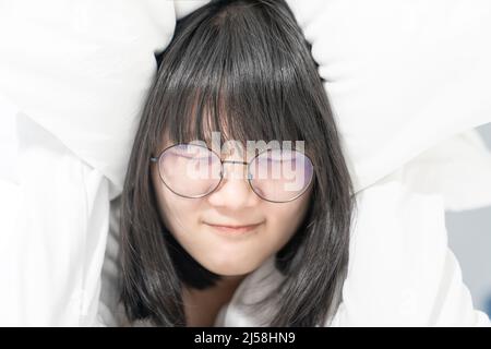 Occhiali donna timido, abash e imbarazzo sotto il cuscino bianco sul letto Foto Stock