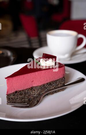 Pezzo di famosa torta di semi di papavero con mousse di lamponi di origine austriaca servito con panna montata e tazza di caffè in vecchio classico caffè-ristorante in Foto Stock