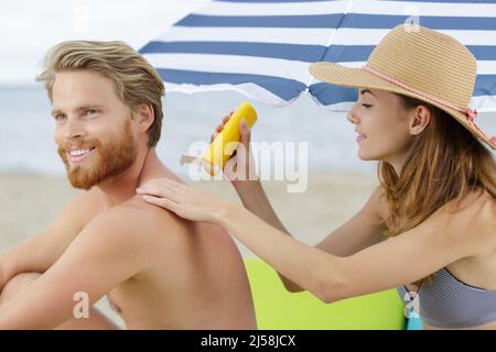 signora che applica crema solare ai suoi partner di nuovo sulla spiaggia Foto Stock