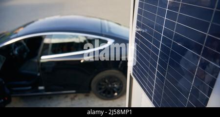 Sullo sfondo sfocato di auto d'élite nera vista ravvicinata di un pannello solare. Concept veicolo elettrico ecologico come alternativa al trasporto a carburante. Foto Stock