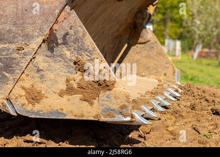 Spianando e livellando un terreno privato. Escavatore giallo che guida la terra in una benna larga Foto Stock