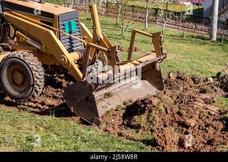 Spianando e livellando un terreno privato. Escavatore giallo che guida la terra in una benna larga Foto Stock