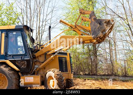 Spianando e livellando un terreno privato. Escavatore giallo che guida la terra in una benna larga Foto Stock