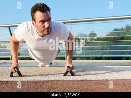 Primo piano di un determinato bell'uomo caucasico di mezza età, atleta che si esercita all'aperto, pompando i muscoli mentre effettua l'addestramento di push-up sull'urb Foto Stock