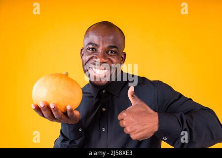 People e Halloween preparazione concetto, uomo che tiene piccola zucca in studio sfondo giallo Foto Stock