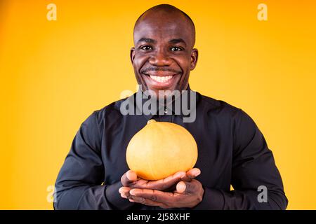 People e Halloween preparazione concetto, uomo che tiene piccola zucca in studio sfondo giallo Foto Stock