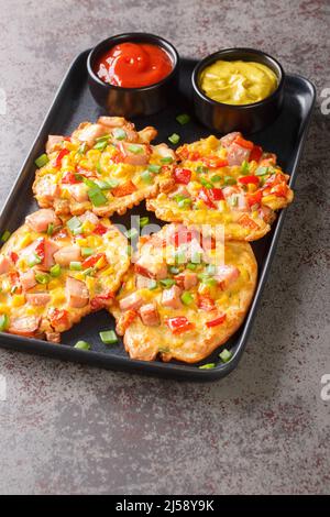 Frittelle con prosciutto, mais, peperoni e cipolle verdi da vicino su un piatto sul tavolo. Verticale Foto Stock