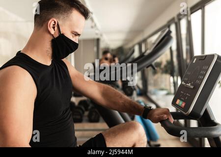 Giovane atletico che indossa una maschera facciale di prevenzione durante il suo allenamento in palestra Foto Stock