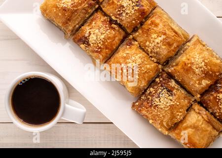 Baklava dolce classica con un piatto di ceramica bianca e una tazza di caffè su un tavolo di legno, macro, vista dall'alto. Foto Stock