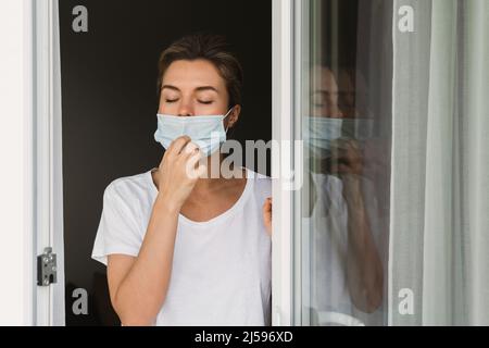 La giovane donna sta andando su un balcone per prendere un respiro profondo perché stava usando la maschera di prevenzione per tutto il giorno Foto Stock