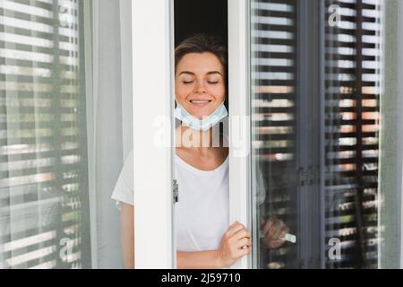 La giovane donna sta andando su un balcone per prendere un respiro profondo perché stava usando la maschera di prevenzione per tutto il giorno Foto Stock