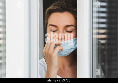 La giovane donna sta andando su un balcone per prendere un respiro profondo perché stava usando la maschera di prevenzione per tutto il giorno Foto Stock