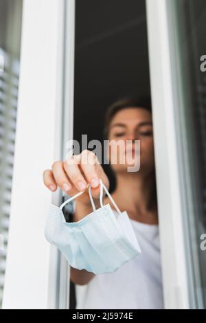 Giovane donna gettando via la maschera di prevenzione usata. Simbolo di fine pandemico. Foto Stock